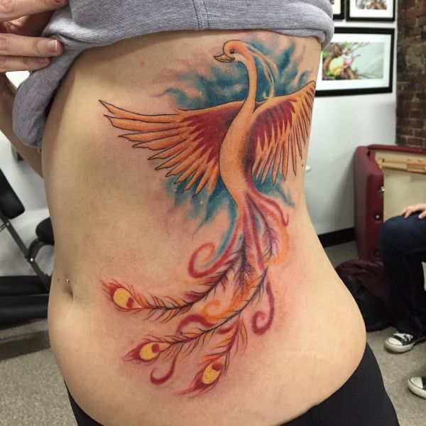 Татуировка жар птица в цвете сбоку тела девушки