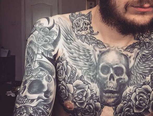 Татуировка на груди в виде черепа, крыльев и цветов