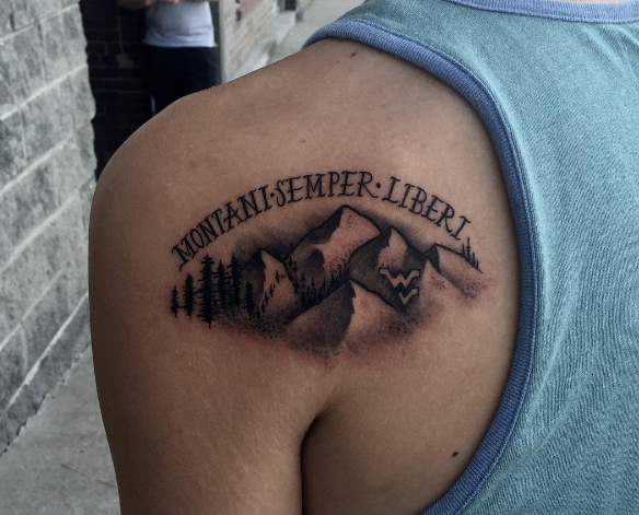 Татуировка гор с надписью на лопатке парня