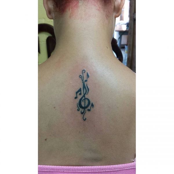 Скрипичный ключ с нотами в виде татуировки на спине девушки