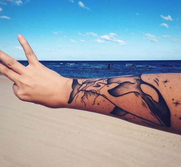Рука с татуировкой кит на фоне моря