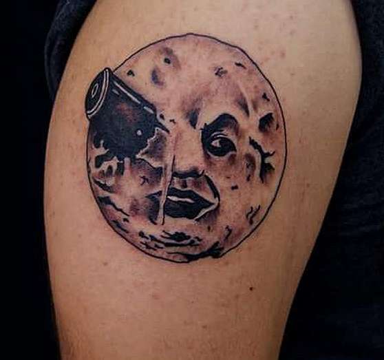 Торчащий предмет из глаза луны: татуировка на плече парня