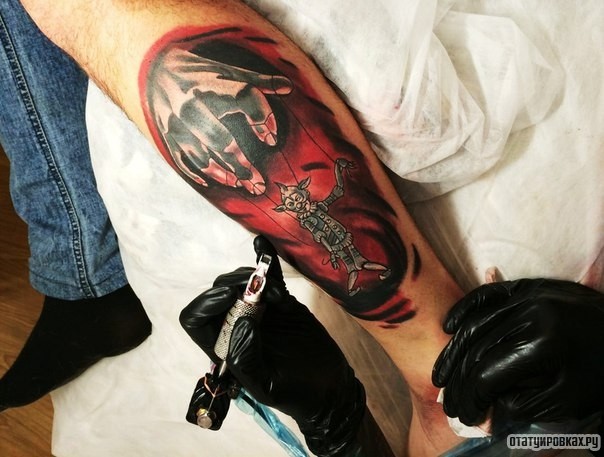 Фотография татуировки под названием «Существо в виде марионетки на красном фоне»