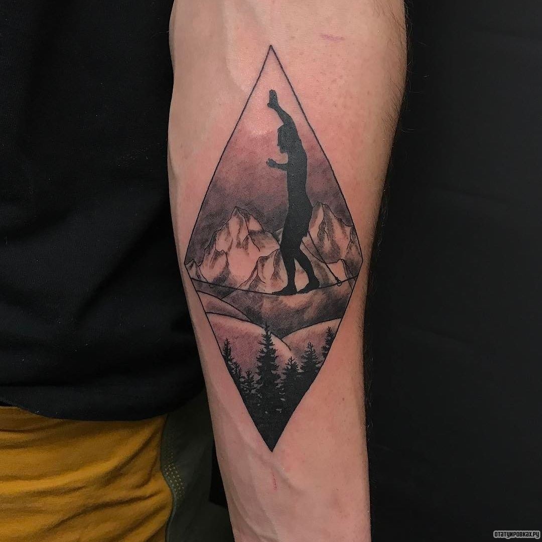 Фотография татуировки под названием «Человек идет по веревке на фоне гор»