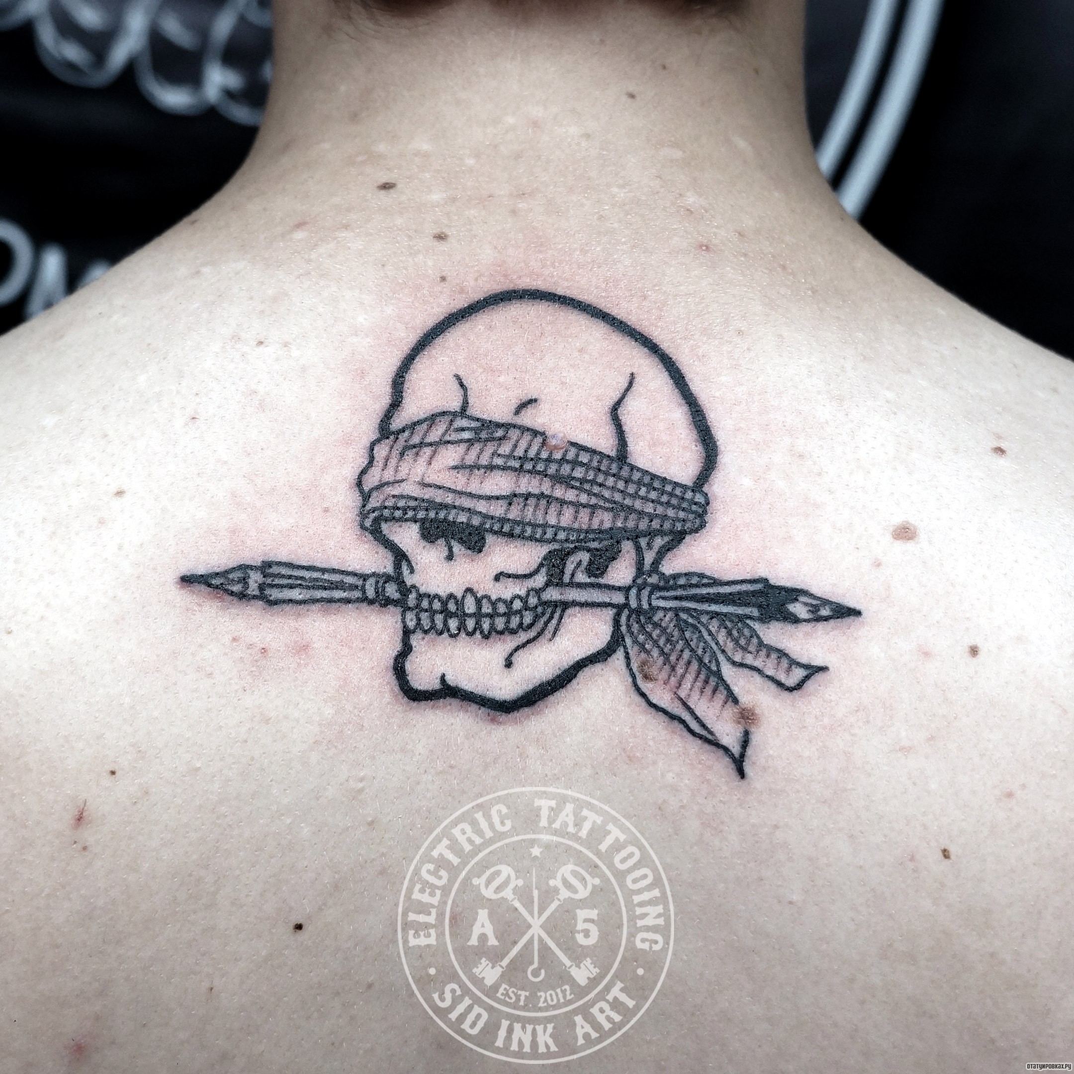 Фотография татуировки под названием «Череп со стрелой в зубах»